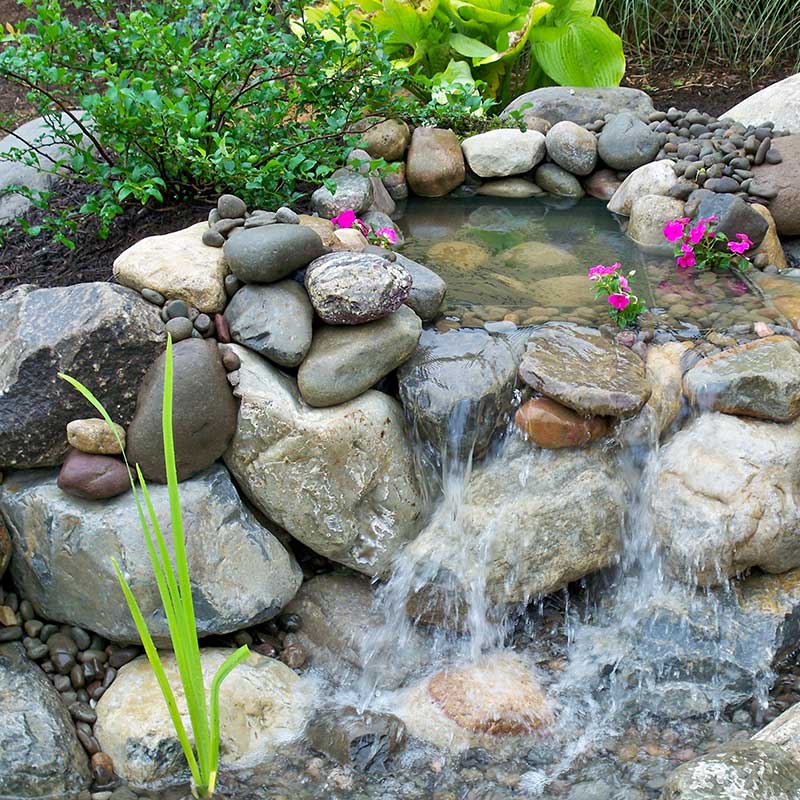 waterfall surrounded by stones in round shape with pink flowers