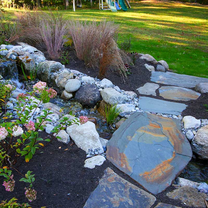 stone garden bridge with waterfall and lawn backdrop with swingset