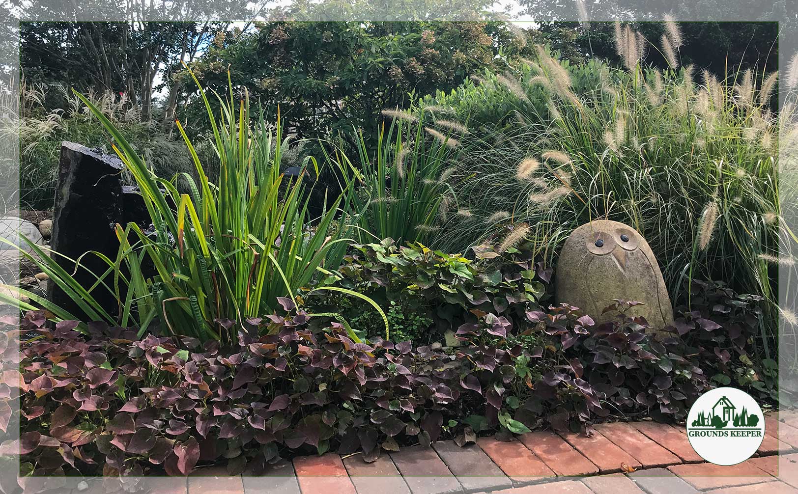 stone owl with tall grasses and purple foliage 